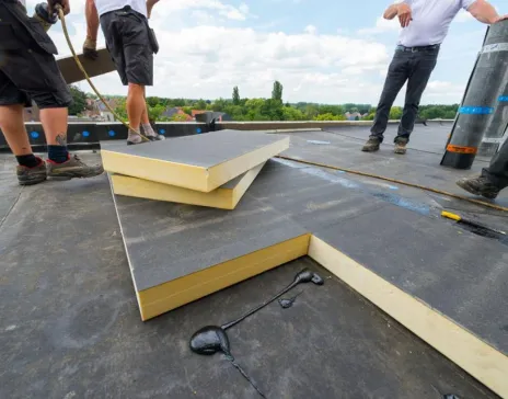 Workers installing insulation panels on a flat roof.