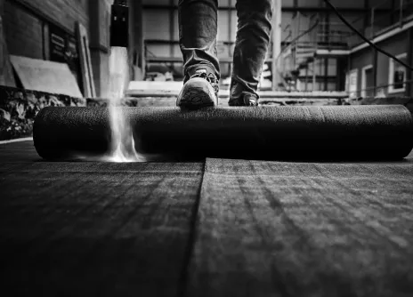 Black and white photo of a person rolling out roofing material indoors.
