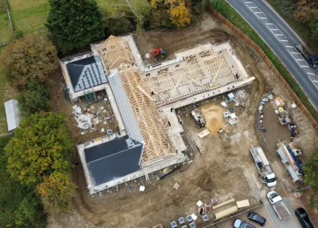 Under-construction building site with vehicles, surrounded by trees and a road.