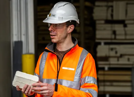 Worker in an orange safety jacket and helmet holding a brick.