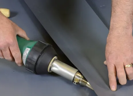 Hands using a heat gun to weld black plastic sheets.