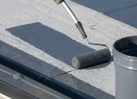 Painting a flat roof with a roller and grey paint.