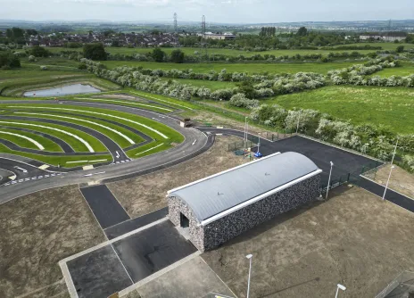 Aerial view of a modern building and landscaped spiral garden, surrounded by green fields.